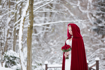 Stunning bride standing in snow covered woods with red cape