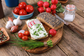 wholemeal roll with quark and fresh chives, radish and tomatoes on a rustic wooden table - healthy breakfast with fresh herbs - close up