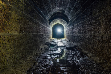 Old vaulted flooded round underground drainage sewer tunnel with dirty sewage water