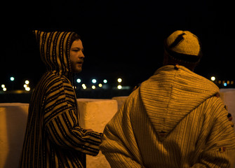 Fototapeta na wymiar Two Man in Traditional moroccan djellaba walking on the street of Asilah Medina, on Atlantic Coast in Morocco. Caucasian with a local Moroccan man