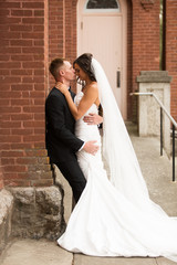 bride and groom leaning against building kissing