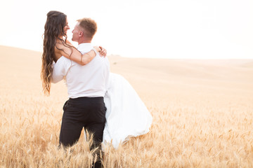 groom carrying bride in wheat field at sunset