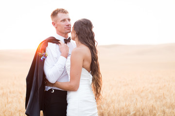 handsome groom holding bride at sunset in wheat field