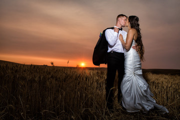Beautiful young couple kissing in front of a dynamic sunset in wheat field