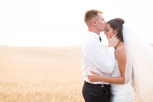 groom kissing bride on forehead in wheat field
