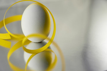 A white egg with yellow ribbon on a silver reflective background. Easter concept. Copy space.