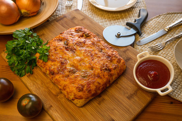 Focaccia bread on a kitchen table with tomatoes, onion, parsley and tomato sauce