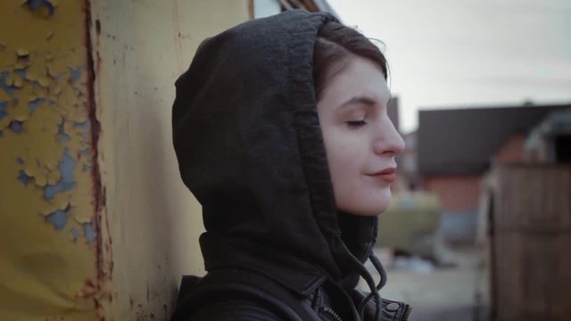 Portrait of young attractive hipster girl in hoodie standing near yellow rusted wall