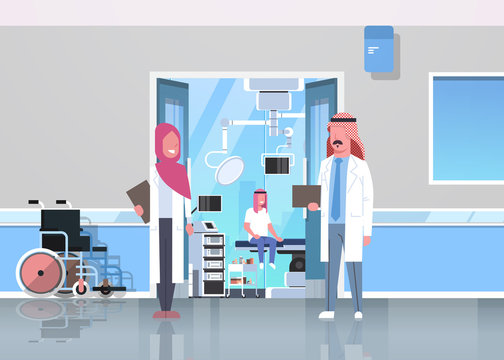 arab doctors discussing in hospital corridor with wheelchair open door to surgery room arabic man sitting operating table modern clinic interior flat full length horizontal