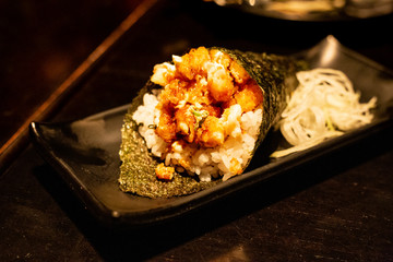 Shrimp temaki sushi on black plate on wood background.