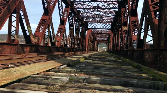 Right pan footage of an old rail road bridge over a river in a small industrial suburban town.