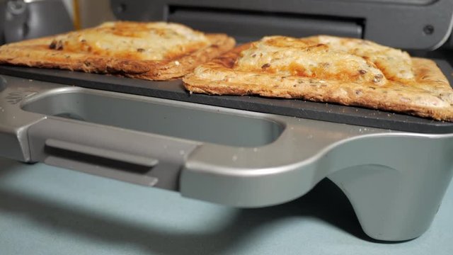 Sandwich maker opens to show a cooked ham and cheese toasty. LOCKED DOWN SHOT. CLOSE UP. WIDE ANGLE.