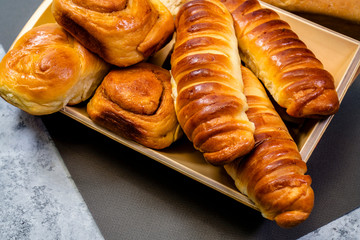 Delicious ruddy homemade buns and pastries of different shapes with cinnamon and various fillings laid out on wooden plate