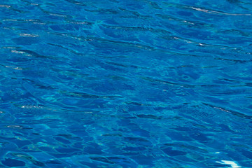 Blue and bright ripple water surface in swimming pool with sun reflection.
