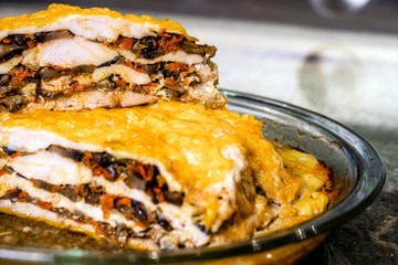 Layered Baked Meat Pie with mushrooms and vegetables topped with melted cheese is on the table in glass tray