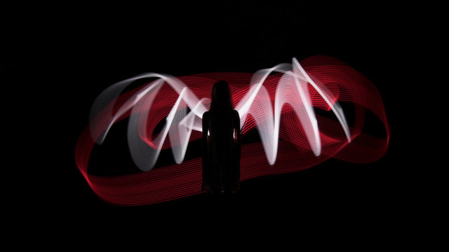 Woman silhouette against red and white backlight in shape of wings. Light painting photography. Long exposure.