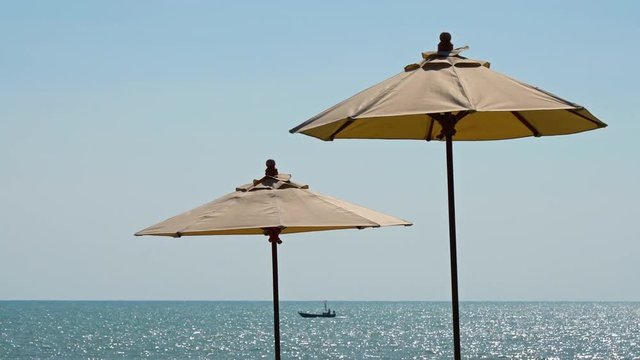 Sun Shade Umbrellas on Windy Beach Afternoon with View of Sea Horizon and Small Boat Passing By