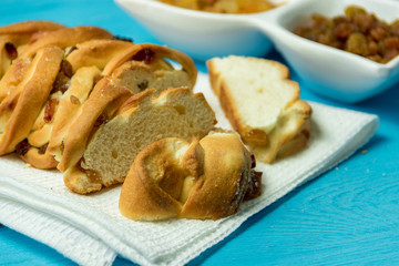 Piece of Sweet Braided Bread with raisins on kitchen towel on blue wooden background.