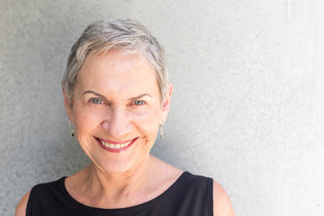 Closeup portrait of beautiful senior woman with grey hair against concrete background (selective focus)