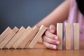 Girl's hand Stopping Falling wooden Dominoes effect from continuous toppled or risk.