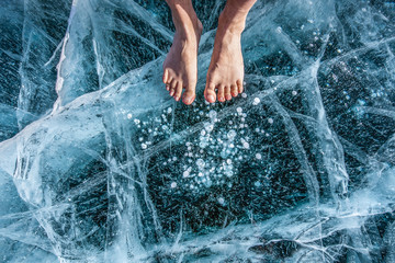 Man foot spa treatment on cracks surface of the natural ice in frozen water at Olkhon Island,...
