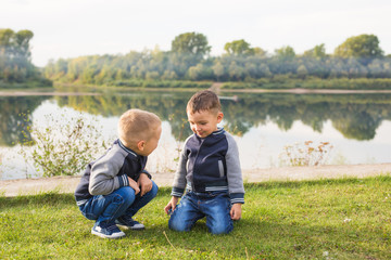 Naklejka na ściany i meble Children and nature concept - Two brothers sitting on the grass over nature background
