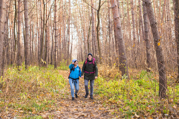 Fototapeta premium Travel, tourism, hike and people concept - Couple with backpacks walking in the autumn forest