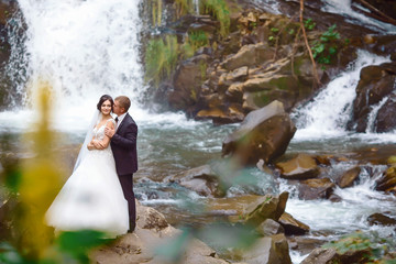 Fototapeta na wymiar young wedding couple of sexy pretty girl or woman with hair in white bride dress and handsome man near beautiful grand waterfall in mountain.