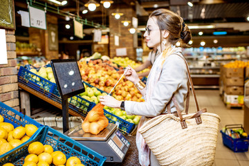 Young woman customer weighing apples packed in eco bag on the scales in the supermarket
