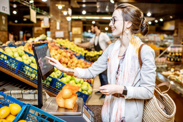 Young woman customer weighing apples packed in eco bag on the scales in the supermarket