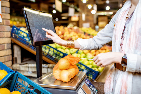 Young woman customer weighing apples packed in eco bag touching the screen of the scales in the supermarket