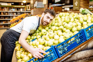 Funny portrait of a handsome shop worker hugging a pile of apples in the supermarket