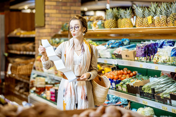 Portrait of a young woman with shocked emotions looking on the long shopping list in the supermarket