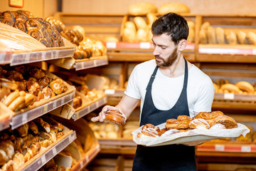 Handsome baker in uniform putting fresh pastries on the shelves in the supermarket