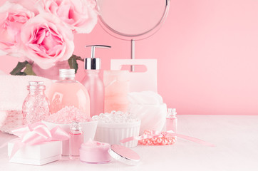 Modern youth bathroom or dressing table design in pastel pink color -  flowers, cosmetic products, bath accessories, jewelry, round mirror on white wood board.