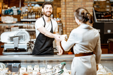 Handsome shop worker selling cheese for a young woman client standing in the supermarket