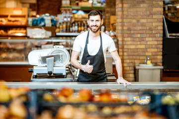 Portrait of a handsome seller or shop worker in apron standing at the counter in the supermarket