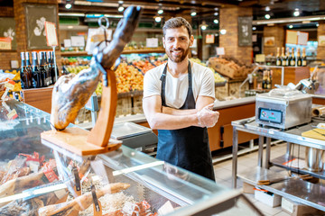 Portrait of a handsome seller standing at the counter with jamon in the supermarket