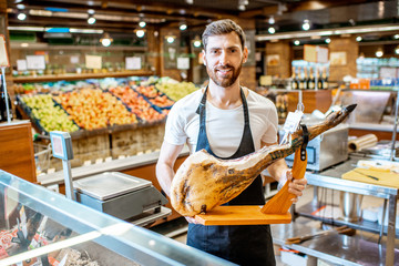Portrait of a handsome seller standing at the counter with jamon in the supermarket