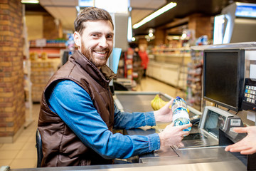 Portrait of a happy and cheerful man as a cashier, sitting at the cash register in the supermarket