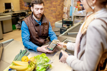 Young woman customer paying with a credit card for shopping at the cash register with cheerful cashier in the supermarket