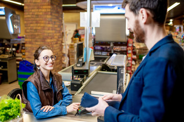 Obraz premium Businessman with happy woman cashier at the cash register buying food in the supermarket