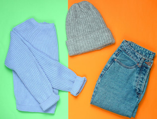 Winter woolen hat, jeans, sweater on a colored paper background, minimalism, top view, flat lay style.