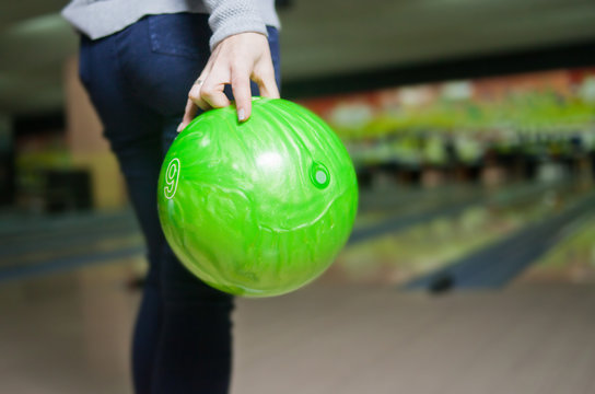 Woman's hand holds green bowling ball ready to throw
