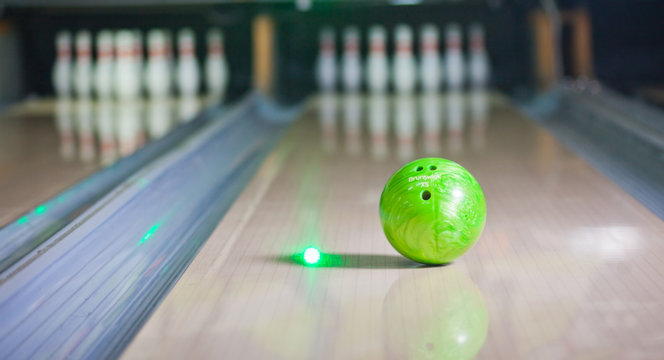 Green Bowling ball put on alley with blurred bowling pin background