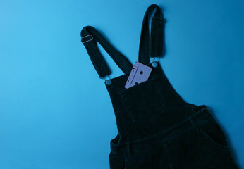 Audio tape in pocket of velveteen overalls on blue neon background. Retro style, music concept, 80s