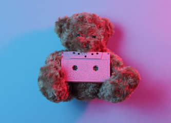 Music lover concept Teddy bear hold audio cassette in red blue neon light. Top view. Retro style 80s. Minimalism