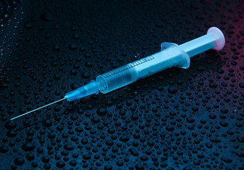 Drug concept, addiction. Syringe on a dark background with water drops. Night life. Neon light