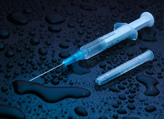 Drug concept, addiction. Syringe on a dark background with water drops. Night life. Neon light
