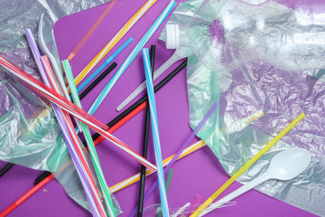 The concept of pollution environment. Cellophane bag, plastic bottle, disposable forks and spoons, cocktail tubes on purple background. Top view